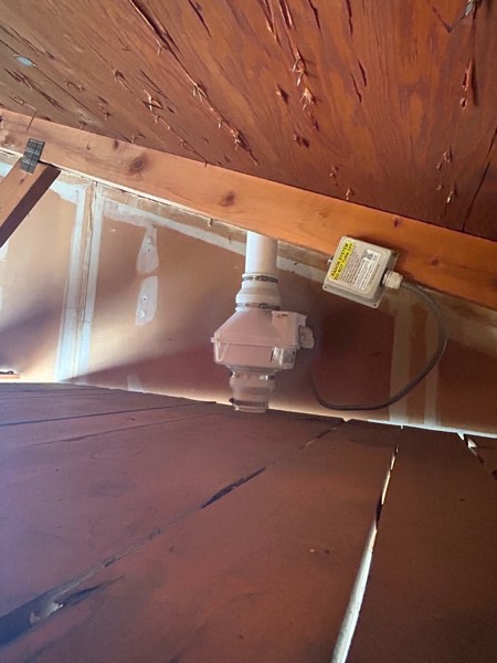 Radon fan mounted in the attic between the roof rafters with its electrical disconnect