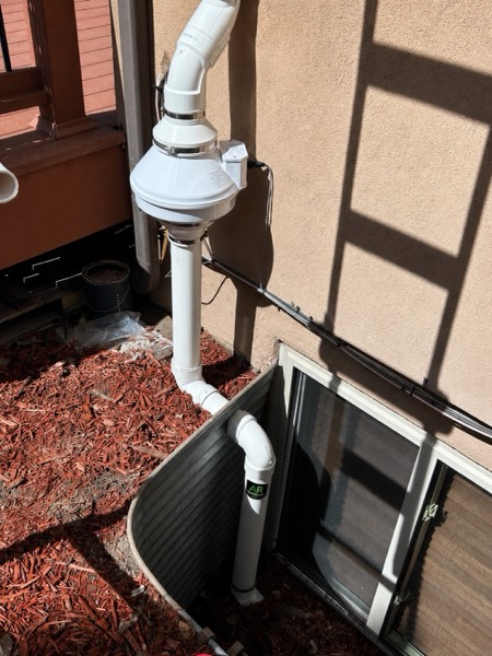 Exterior radon fan mounted above a window well on a stucco home