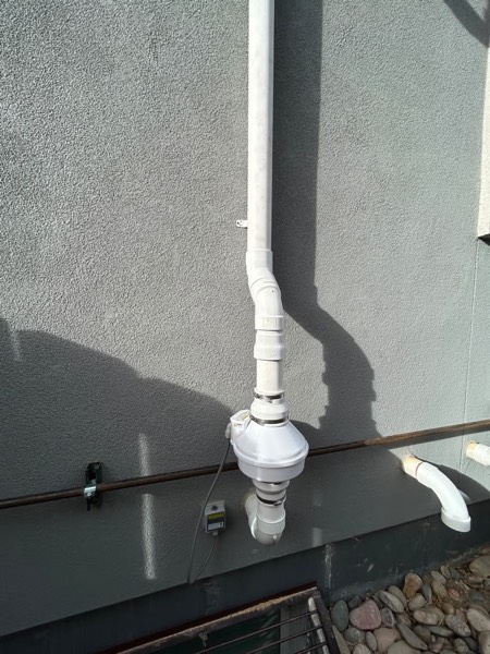 Exterior radon fan and vent on a grey stucco wall with the electrical disconnect fitted