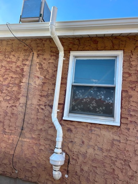 Exterior radon fan and vent on a textured stucco wall beside a window