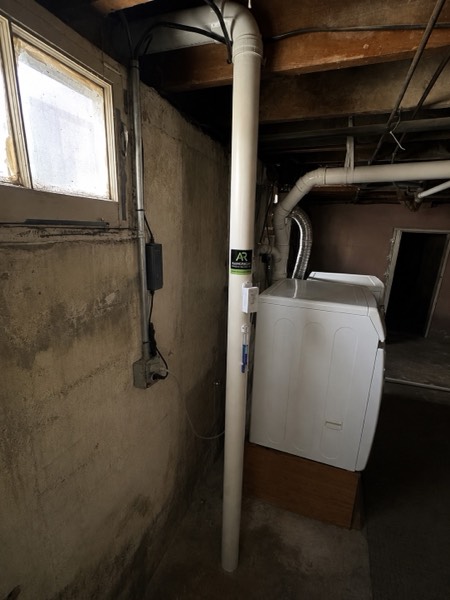 Radon mitigation pipe running floor to ceiling in a basement beside the laundry